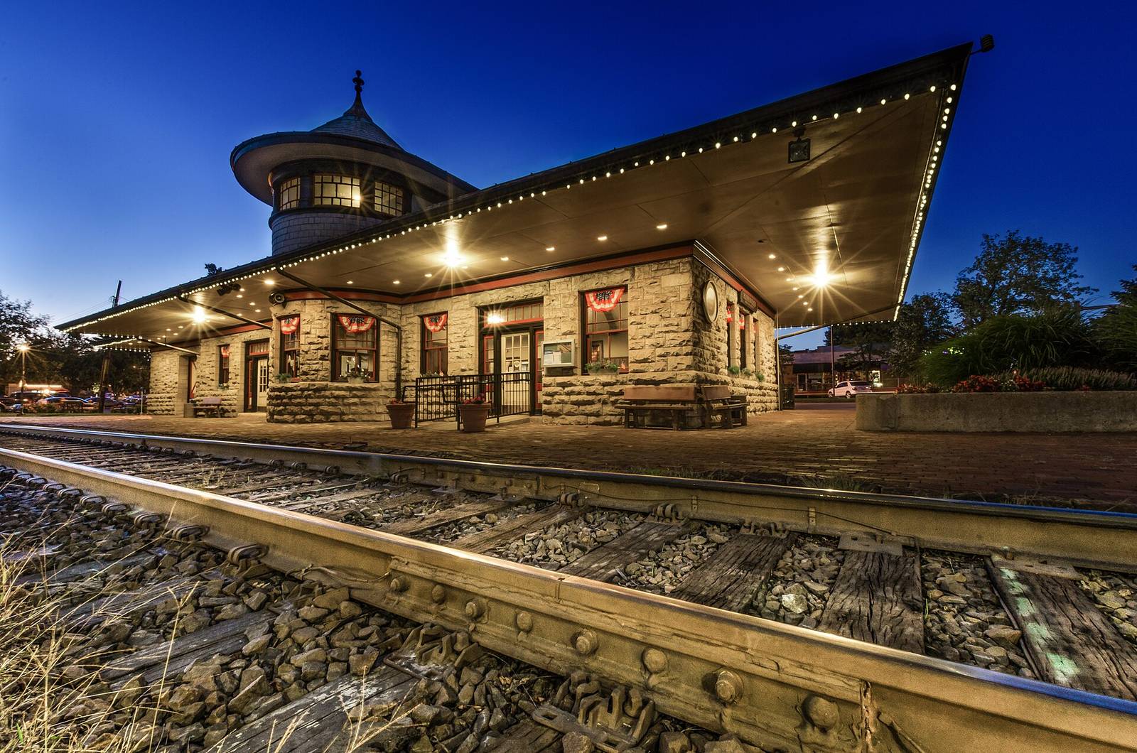 The stone Kirkwood train station at blue hour, its round tower and lit eaves beside the tracks.